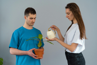 Woman watering plant while it is being carried by a man