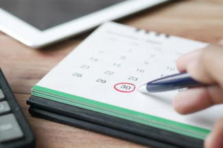Paper calendar with person holding pen and a circle around a specific date.